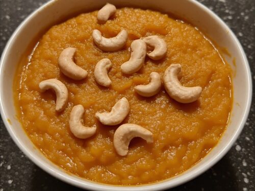Warm carrot halwa with a vibrant red color, topped with crushed cashews and almonds