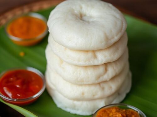 Soft white steamed idlis arranged on a banana leaf